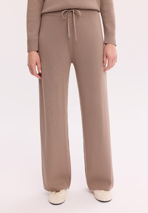 Beżowe szerokie dziergane spodnie z regulowanym sznurkiem w pasie, noszone z dopasowanym długim rękawem i białymi butami na co dzień.