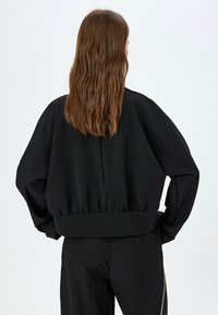 Felpa nera a maniche lunghe, corta, con materiale testurizzato a coste, spalle scese e orlo arricciato. Presenta una vestibilità comoda e rilassata.
