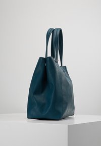 Tyrkysově modrý kožený taška přes rameno s jemnou texturou, prostorným designem, dvěma prodlouženými uchy a uvolněným střihem. Žádné viditelné kovové prvky.