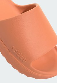 Sandalo scivolo in gomma color corallo con superficie texturizzata, cinturino largo e logo in rilievo. Presenta una soletta sagomata e suola scanalata.