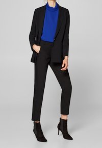Blazer nero su misura, dolcevita blu aderente e pantaloni neri slim, abbinati a stivaletti neri alla caviglia con un pannello laterale texturizzato.