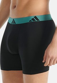 Černé boxerky vyrobené z elastického materiálu, s tyrkysovým elastickým pasem a černým geometrickým logem.