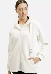 Biały rozpinany hoodie z kapturem, bocznymi kieszeniami i akcentem logo z przodu. Miękka tkanina z prążkowanymi mankietami i luźnym krojem.