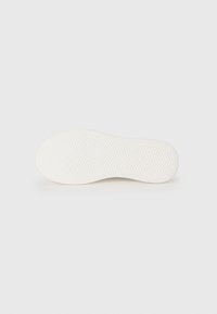 Hvid sneaker sål med en tekstureret overflade og zigzagmønster. Rundede kanter og glat gummimateriale. Rent og minimalistisk design.