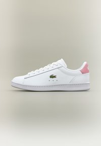 Baltas sneakers ar rozā zamša akcentu uz papēža, apaļa pāļa dizains, auklu priekšpuses, un zaļš izšūts krokodila logotips sānos.