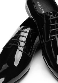 Czarne lakierowane buty wizytowe ze skóry lakierowanej o błyszczącym wykończeniu, z zapięciem na sznurowadła i smukłą sylwetką. Subtelne przeszycia na cholewce.