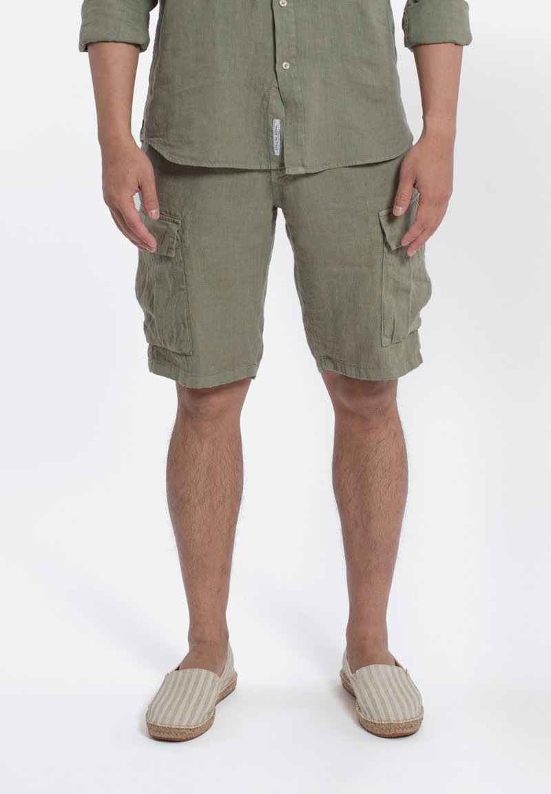 Camicia in lino e pantaloni cargo color verde oliva, con tasche applicate. Espadrillas beige a righe con suola intrecciata. Vestibilità pulita e casual.