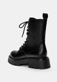 Bottine en cuir noir avec une surface texturée, à lacets à l'avant, bout rond et semelle en caoutchouc épaisse. Comprend une languette à l'arrière.