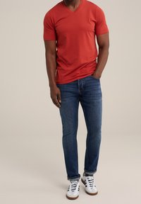 Röd t-shirt med v-hals, korta ärmar, ihop med medelblå jeans och vita sneakers med bruna accenter. Enkel design, tät passform.