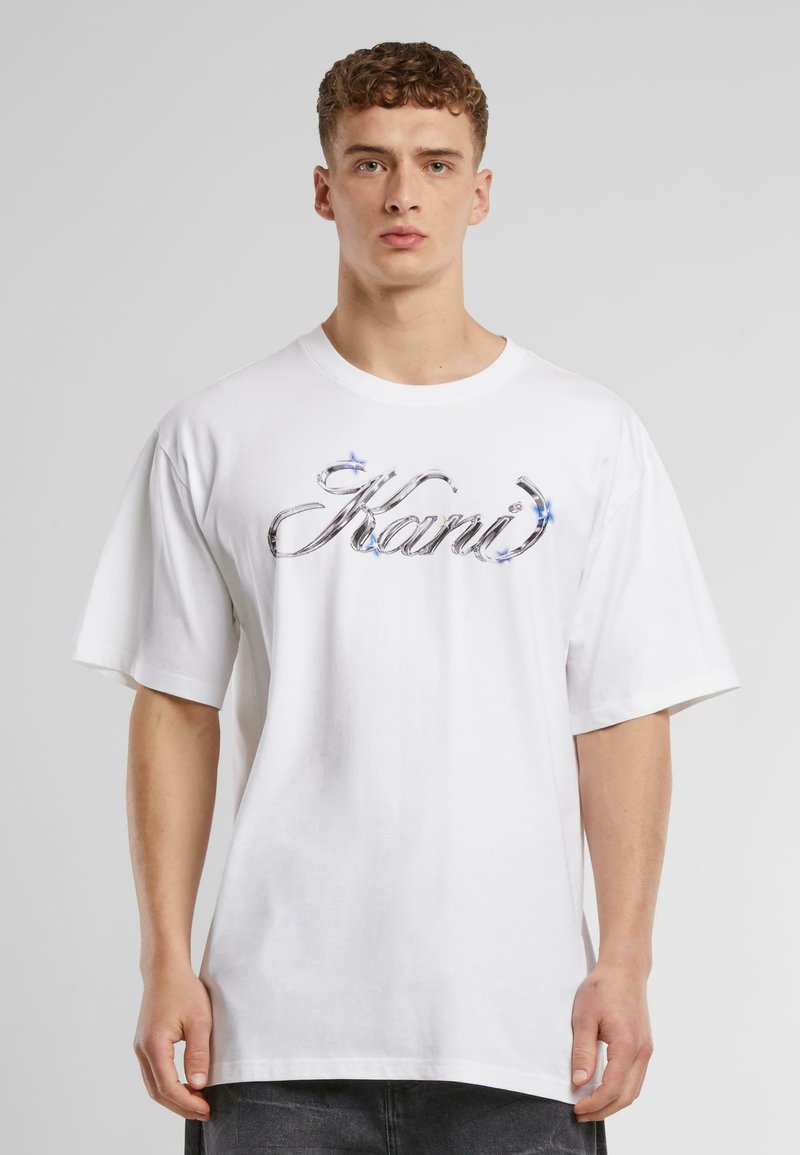 White cotton t-shirt with short sleeves, featuring a large, metallic silver logo "Kani" embellished with blue accents on the front.