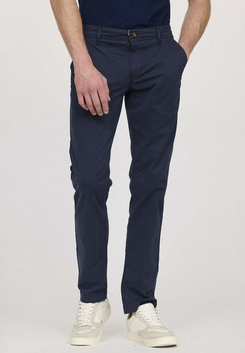 Chino bleu marine en coton avec une coupe slim, présentant une fermeture à bouton, des passants de ceinture et des poches latérales, associés à des baskets blanches.