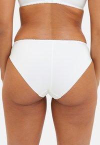 Culottes blanches avec une texture lisse, ornées d'une finition en dentelle le long de la taille et des ouvertures de jambe, avec une coupe haute pour le confort.