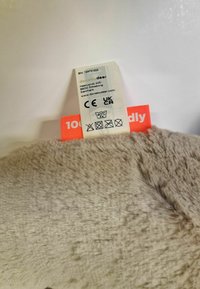 Plysset stof i beige med en blød tekstur. Plejemærke vedhæftet, som angiver 100% genanvendte materialer og vaskeanvisninger.