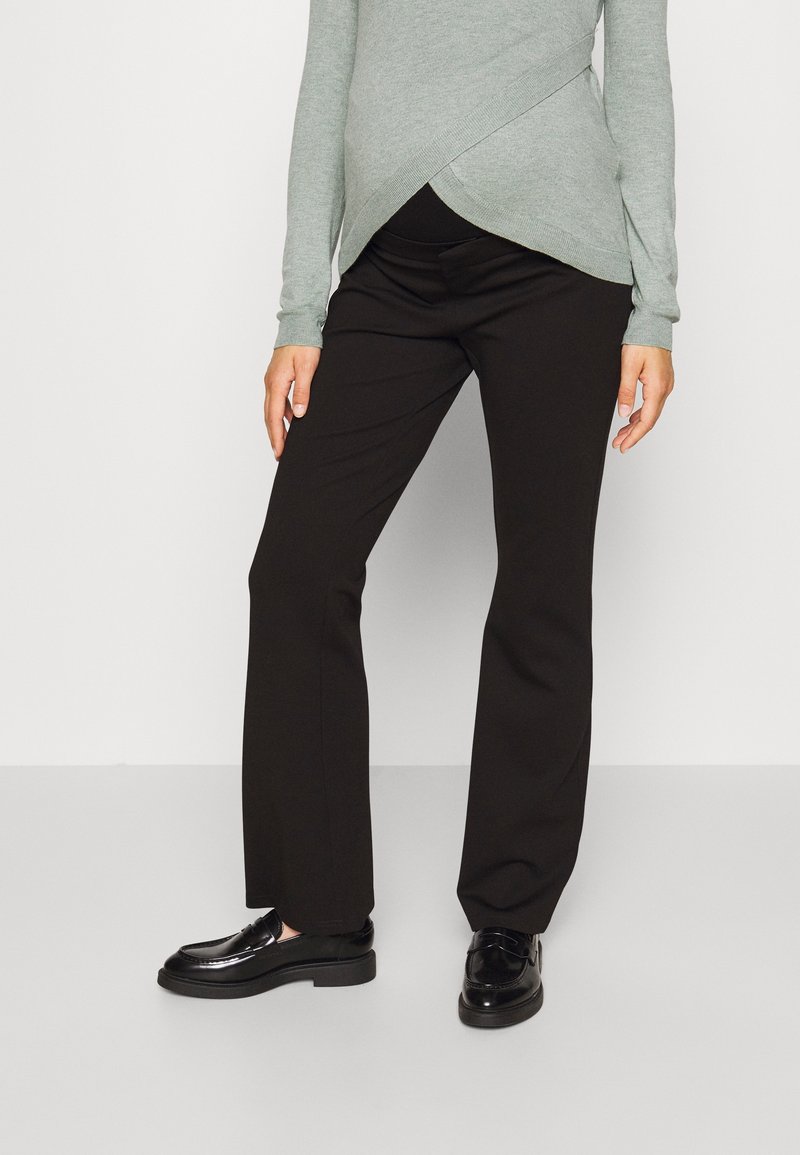 Zwarte op maat gemaakte broek met een rechte pijp, gecombineerd met een grijze top met lange mouwen en een asymmetrisch ontwerp. Zwarte glanzende schoenen maken de look compleet.