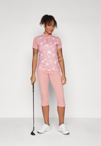 Ροζ πολο γκολφ με φλοράλ σχέδιο, συνδυασμένο με καπιρί παντελόνια. Ελαφρύ ύφασμα, κοντά μανίκια και κλασικό γιακά, με λευκά αθλητικά παπούτσια.