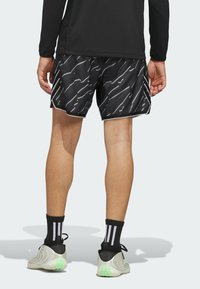 Mustat urheilushortsit, joissa on sahalaitainen harmaa kuvio, valkoinen reuna ja sivuaukko. Yhdistetty mustiin sukkiin, joissa on kaksi valkoista raitaa, ja vaaleanharmaisiin kenkiin.