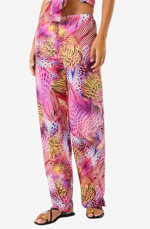 Donna che indossa pantaloni a gamba larga e top abbinato in vivaci colori rosa, giallo e viola con stampa animalier astratta e sandali neri.