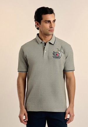 Polo gris con ribetes en azul marino, que presenta un logotipo en el pecho. Mangas cortas, cuello tradicional y corte recto en el dobladillo.