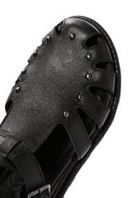 Infradito in pelle nera con design a intaglio, adornati con borchie nere lucide. Presentano una fascia regolabile e una suola texturizzata per una migliore presa.