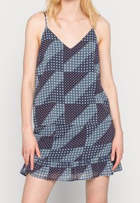 Blommönstrad klänning med V-ringning och tunna remmar. Har blåa, marinblå och vita geometriska mönster samt en volangkant längst ner.