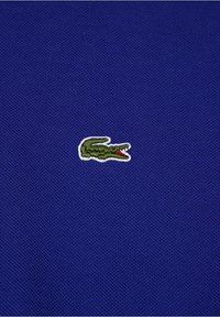 Gros plan sur un petit logo de crocodile vert brodé sur un tissu bleu texturé.