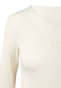 T-shirt crema a maniche lunghe con scollatura a V, con bordo in pizzo sul collo. Tessuto morbido con una texture liscia. Adatto per l'abbigliamento casual.