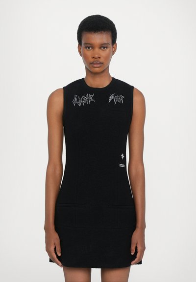 Robe sans manches noire au design ajusté. Présente un texte décoratif blanc, deux poches avant et un détail graphique d'étoile près de l'ourlet.