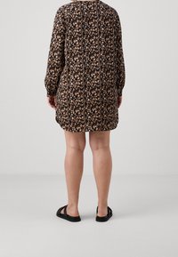 Abito nero con motivo floreale in tonalità pesca e crema, dotato di maniche lunghe e vestibilità ampia, abbinato a sandali neri.