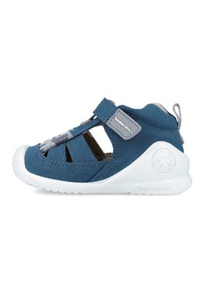 Sandalia de tela azul con diseño recortado, suela de goma blanca, correa ajustable, acentos grises y logo en el talón, adecuada para niños.