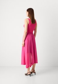 Rožinė be rankovių suknelė su lengva, plazdančia sijonu ir elastinga juosmens juosta. Dėvima su juodais aukštakulniais sandalais, styled iš nugaros.