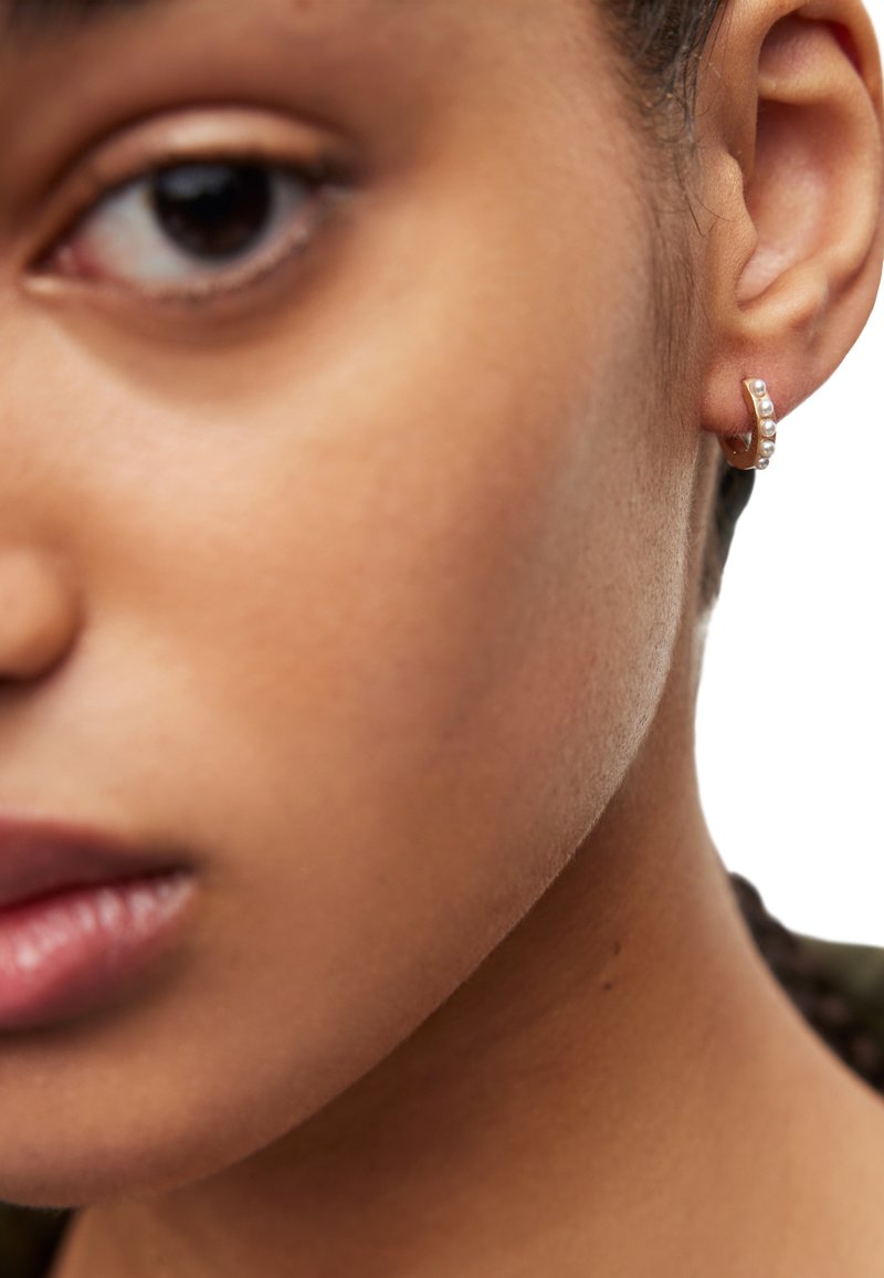 Orecchino a cerchio d'oro con cinque piccole perle bianche, indossato all'orecchio. La vista ravvicinata mette in evidenza il design dell'orecchino e la texture della pelle.