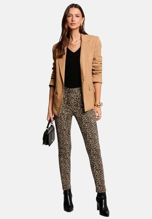 Blazer marrón sobre una blusa negra, combinado con pantalones ajustados de estampado de leopardo. El conjunto se completa con botas negras hasta el tobillo y un pequeño bolso negro.
