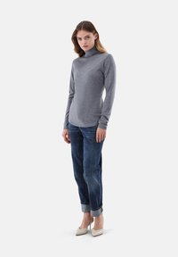 Grauer Rollkragenpullover im schicken Design, kombiniert mit dunkelblauen Jeans mit umgekrempeltem Saum und beigefarbenen spitzen High Heels. Glatte Textur.