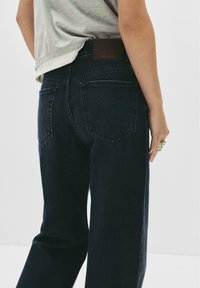 Mörk tvättade denimjeans med rak bendesign, med två bakfickor och en brun etikett vid midjan. Mjuk textur.