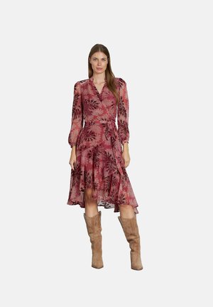 Vestido envolvente rojo con flores, de manga larga, con dobladillo con volantes, tejido ligero y cintura ceñida. Combinado con botas taupe hasta la rodilla.