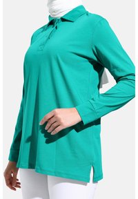Polo shirt turchese a maniche lunghe con colletto, pettorina frontale e spacco sui lati. Realizzato in un tessuto liscio e leggero.