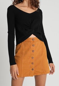Svart ribbad långärmad topp med en framvridning, tillsammans med en högmidjad orange denimkjol med knäppning fram.