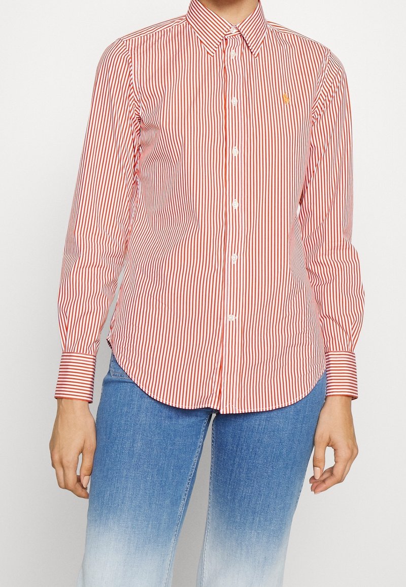 Red and white striped button-up shirt, cotton material, long sleeves, classic collar, features a small logo on the chest, curved hem.