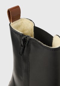 Botim de cano baixo em couro preto com fecho de correr, alça de puxar em couro castanho e forro macio texturizado.