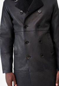 Black leather double-breasted coat with a textured collar, featuring six front buttons and side pockets. Smooth finish, modern design.