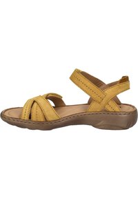 Sandale en daim jaune avec un design de brides croisées, une semelle intérieure rembourrée et une semelle en caoutchouc flexible et texturée. Talon bas pour le confort.