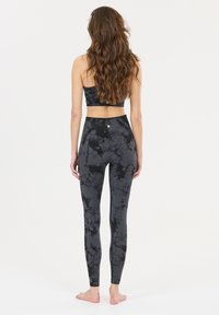 Ensemble de sport tie-dye noir comprenant un top court et un legging taille haute, tous deux fabriqués en tissu extensible avec une texture lisse.