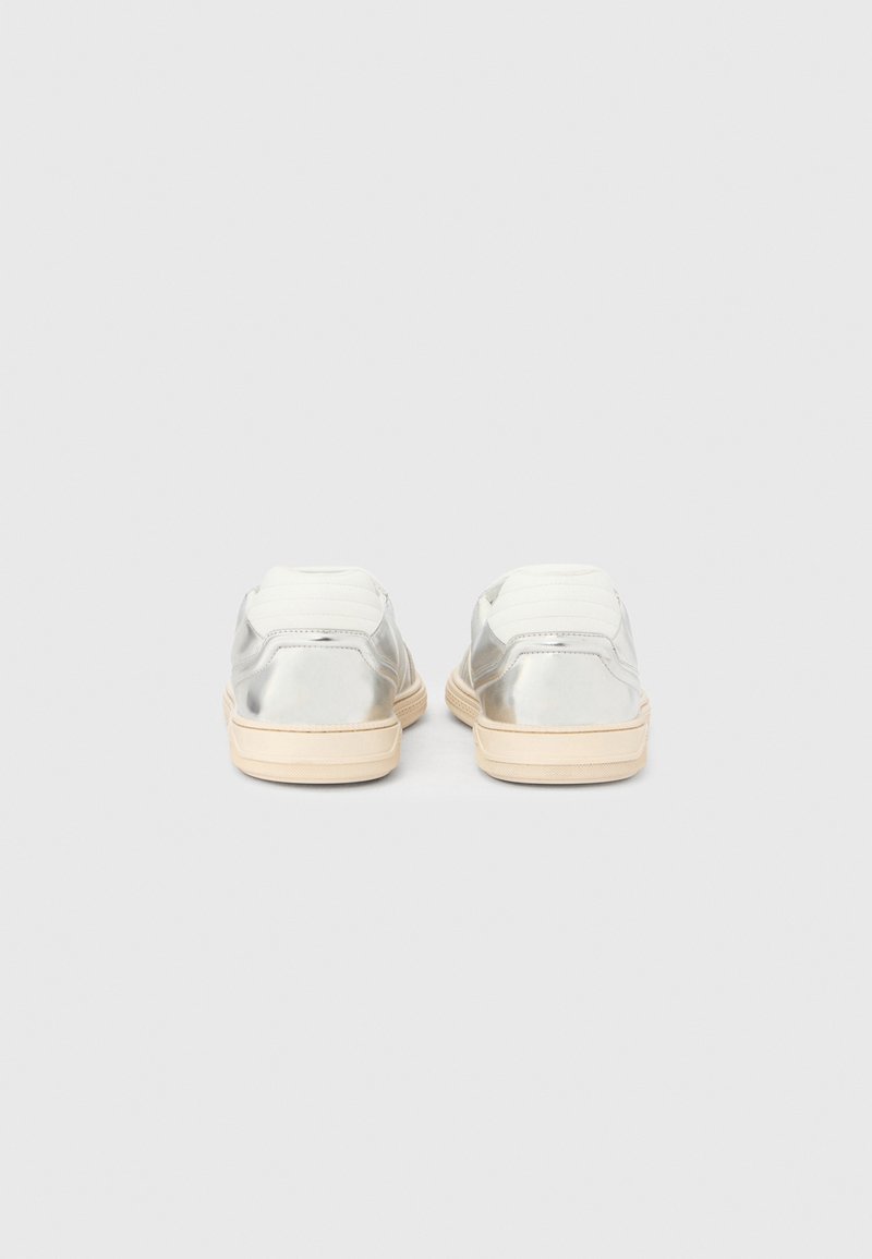 Sneakers in metallo argentato con dettagli in tessuto bianco, punta tonda e suola in gomma beige, caratterizzate da una texture liscia e senza motivi visibili.