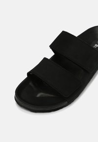 Sandale noire à glissière en daim avec deux brides réglables. Dotée d'une semelle texturée et d'un fond de chaussure incurvé pour le confort.