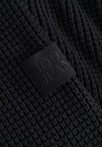 Zbliżenie czarnej dzianiny z czarną wplecioną metką z napisem "JOOP JEANS" naszytą na materiale.