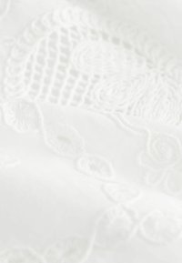 Țesătură albă cu broderie reliefată complexă, având modele florale și spirale, evidențiind o textură moale și un finisaj neted.
