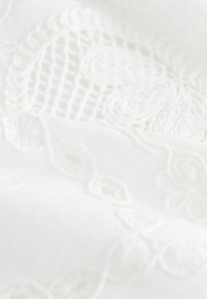 Weißer Stoff mit filigraner erhabener Stickerei in Blumen- und Wirbelmustern, der eine sanfte Textur und ein glattes Finish präsentiert.