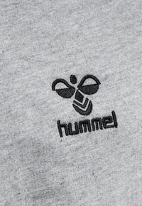 Tessuto di cotone grigio con un logo ricamato in nero di un'ape stilizzata sopra il testo "hummel". Texture sottile con trama del tessuto visibile.