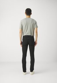 Camiseta gris de manga corta con cuello redondo, combinada con jeans negros ajustados que tienen bolsillos traseros y una cinturilla oscura, llevada con zapatillas blancas.