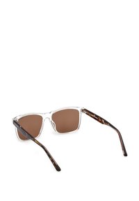 Kirkkaat kehykset aurinkolasit ruskeilla linsseillä, hieman ylisuuret neliömuodot, joissa on tumman kilpikonnakuosiset varsiosat.